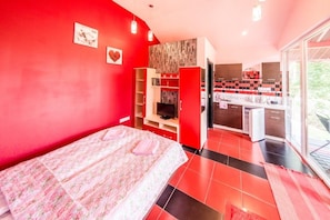Ein modernes Hotelzimmer in Rot gehalten, mit Bett, Fernseher, Küchenzeile und Balkon mit Blick.