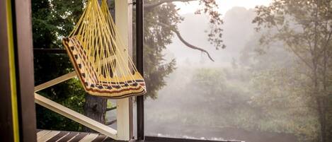 A wooden deck with a hanging yellow hammock and a view of a forested area through a window.