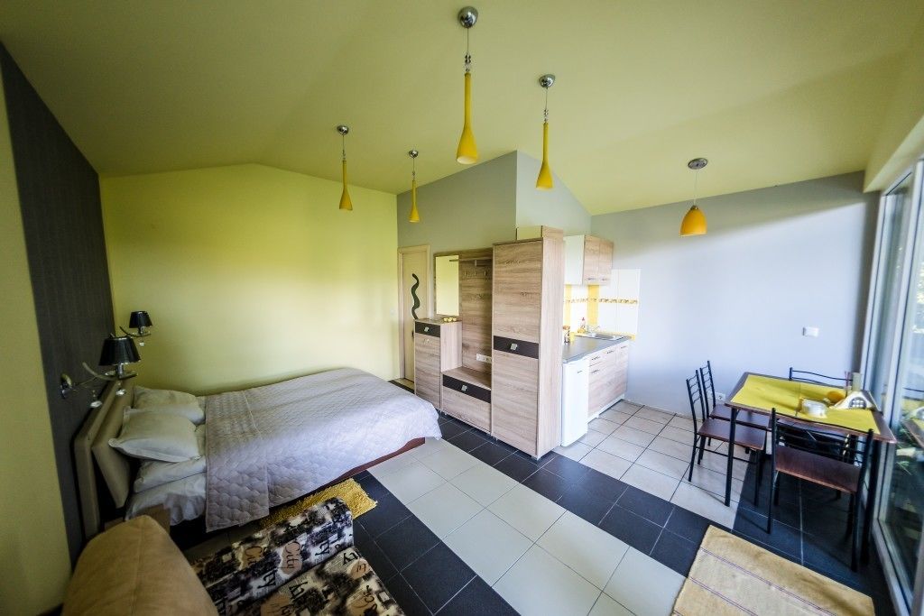 A bedroom with a bed, bedside table, lamp, and a view of a dining area with a table and chairs.