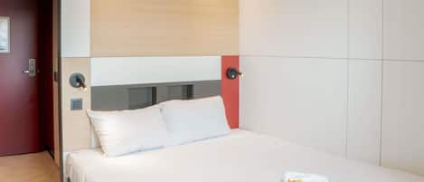 Ein modernes Hotelzimmer mit einem Bett, einem Nachttisch und einer wandmontierten Bedieneinheit.