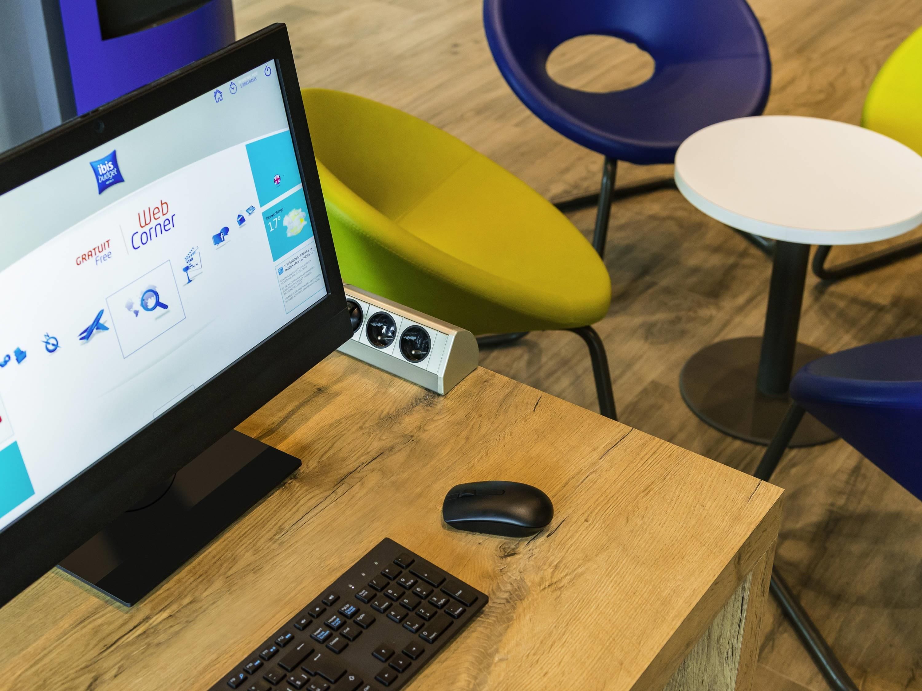 A computer desk with a monitor, keyboard, and mouse, surrounded by colorful chairs and a small table.