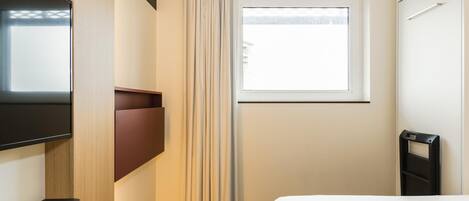 A hotel room with a bed, a TV mounted on the wall, a window with curtains, and a door with a handle.