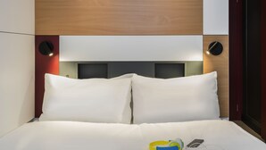 A neatly made bed with white linens, a smartphone, and a yellow and blue object on the bed. - ibis budget Blankenberge (Blankenberge)