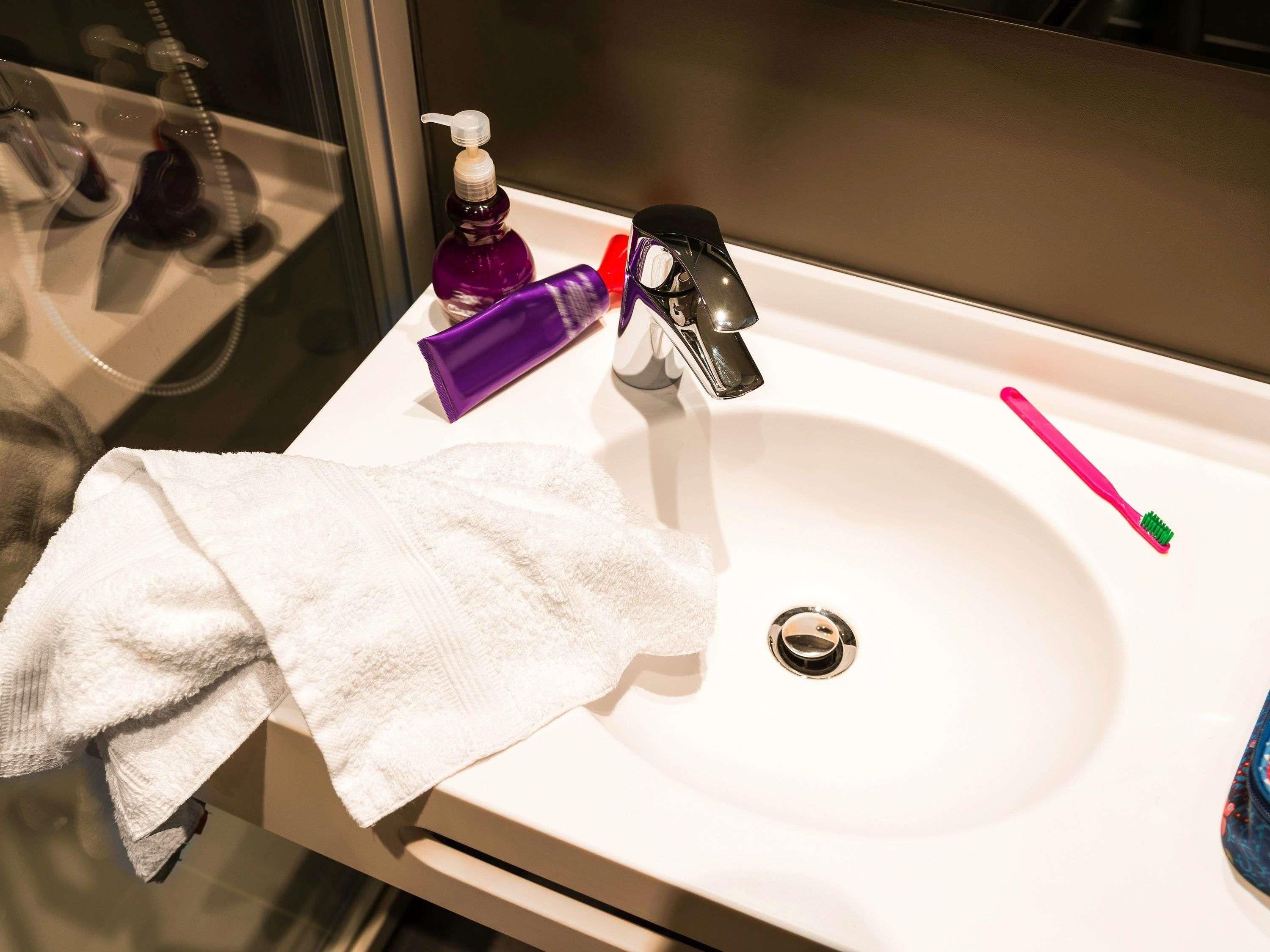 A bathroom sink with a white towel, a purple bottle, a pink toothbrush, and a faucet.