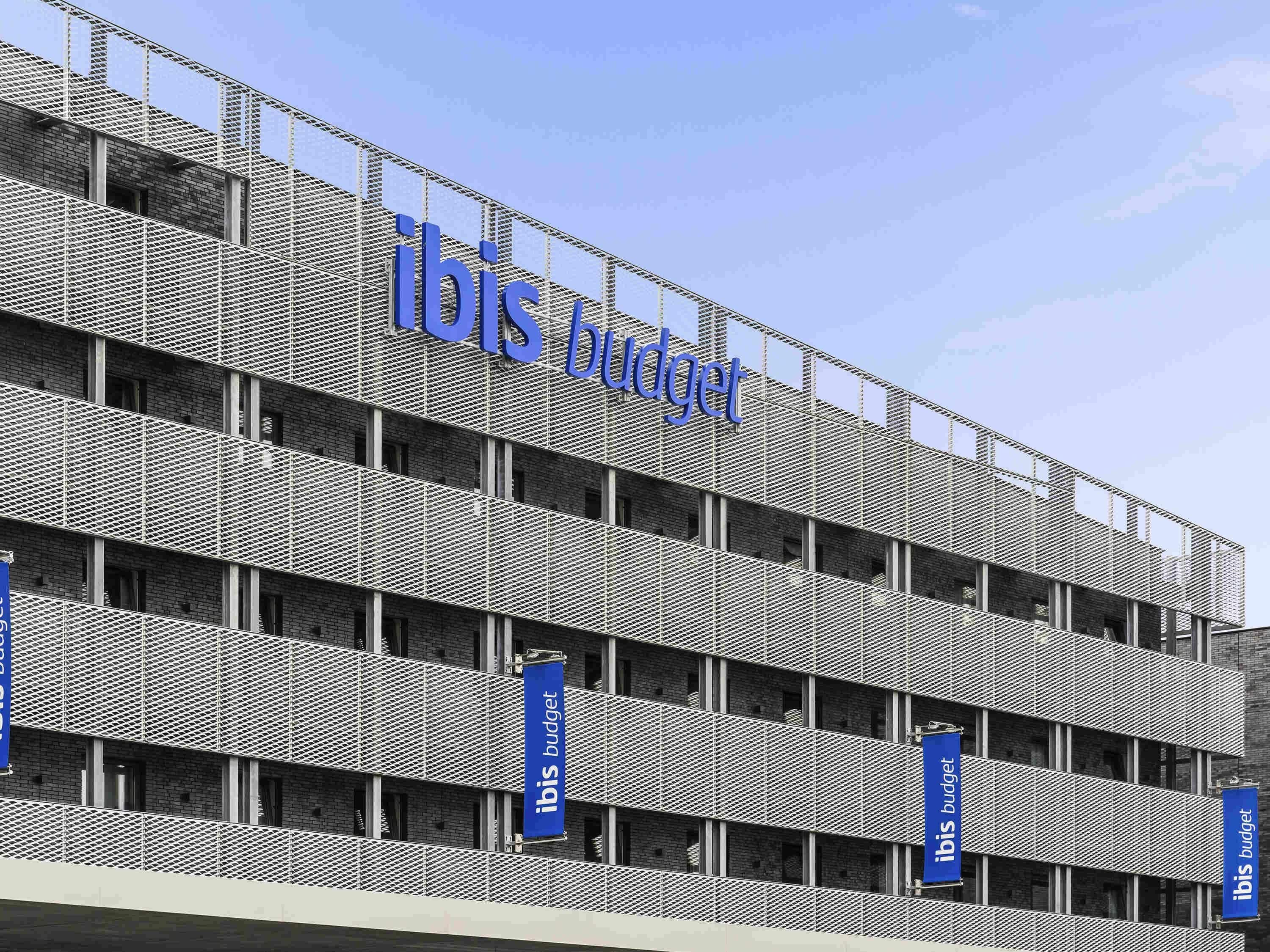 Un immeuble à plusieurs étages doté d’une façade en treillis métallique et de l’enseigne « ibis budget ».