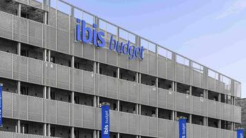 Un immeuble à plusieurs étages doté d’une façade en treillis métallique et de l’enseigne « ibis budget ».