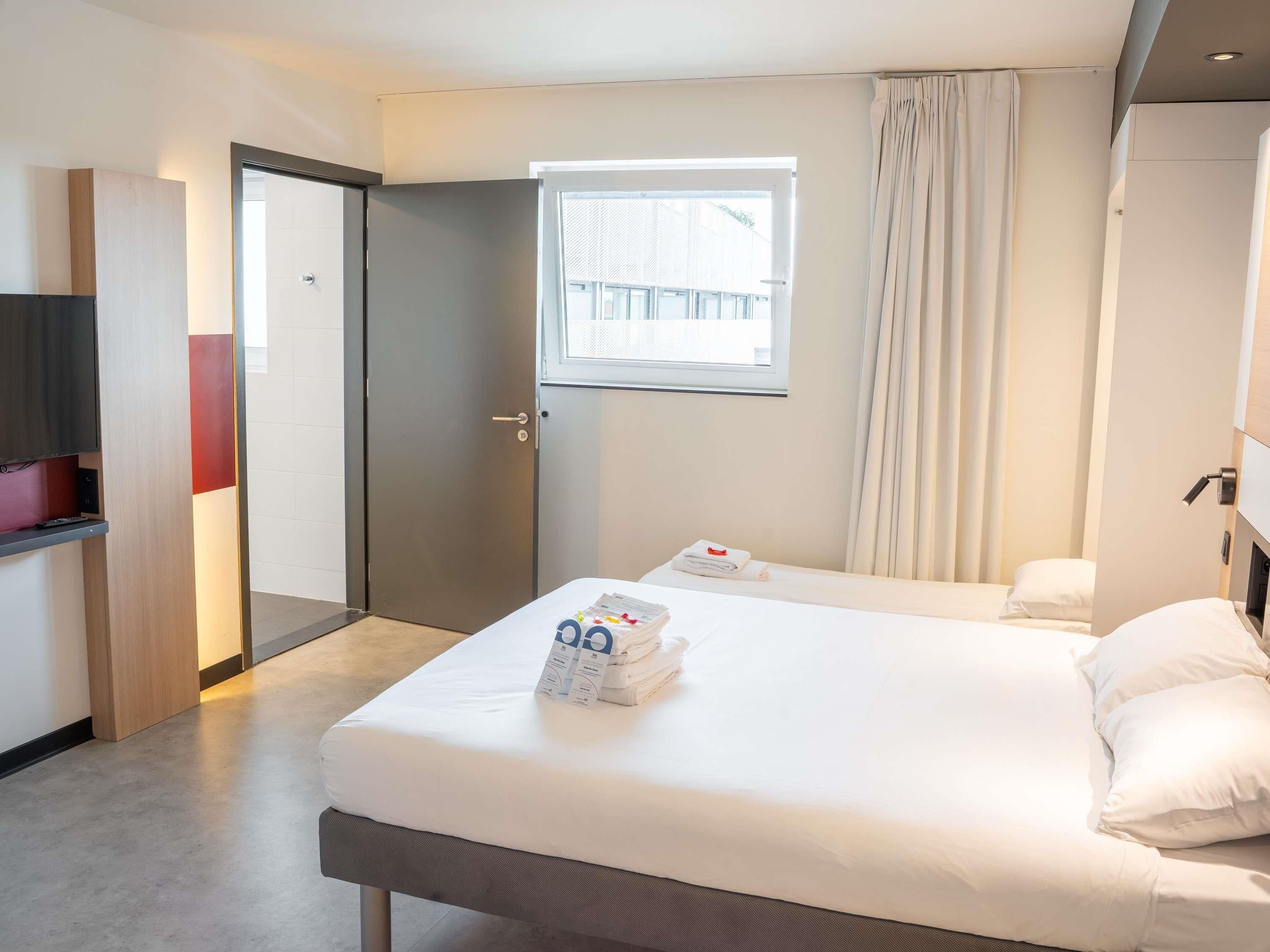 Una habitación de hotel con una cama, una ventana, una puerta y un televisor.