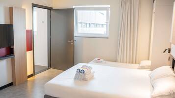 Una habitación de hotel con una cama, una ventana, una puerta y un televisor.