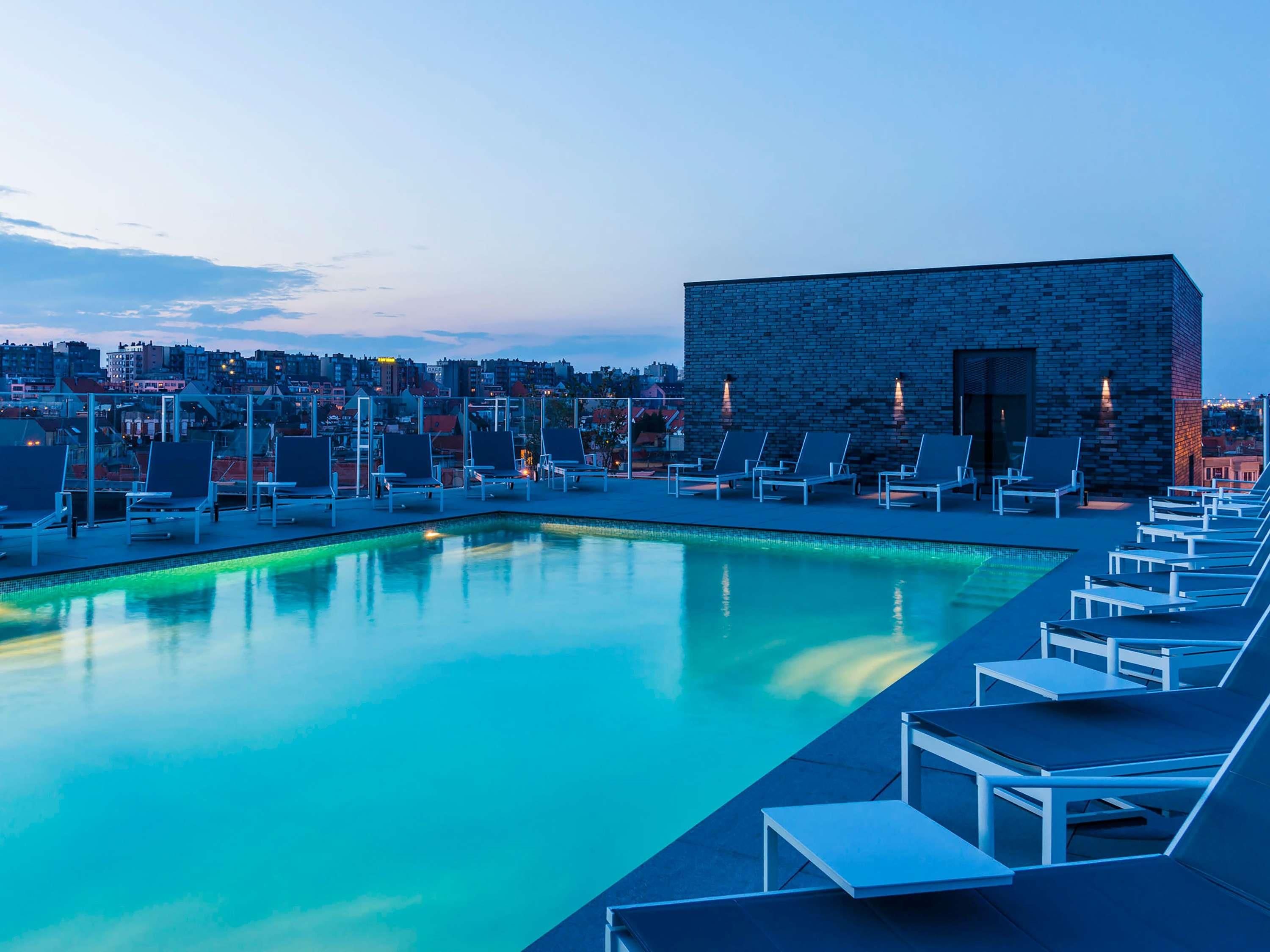 Una piscina en la azotea con sillones de descanso y un edificio de piedra.