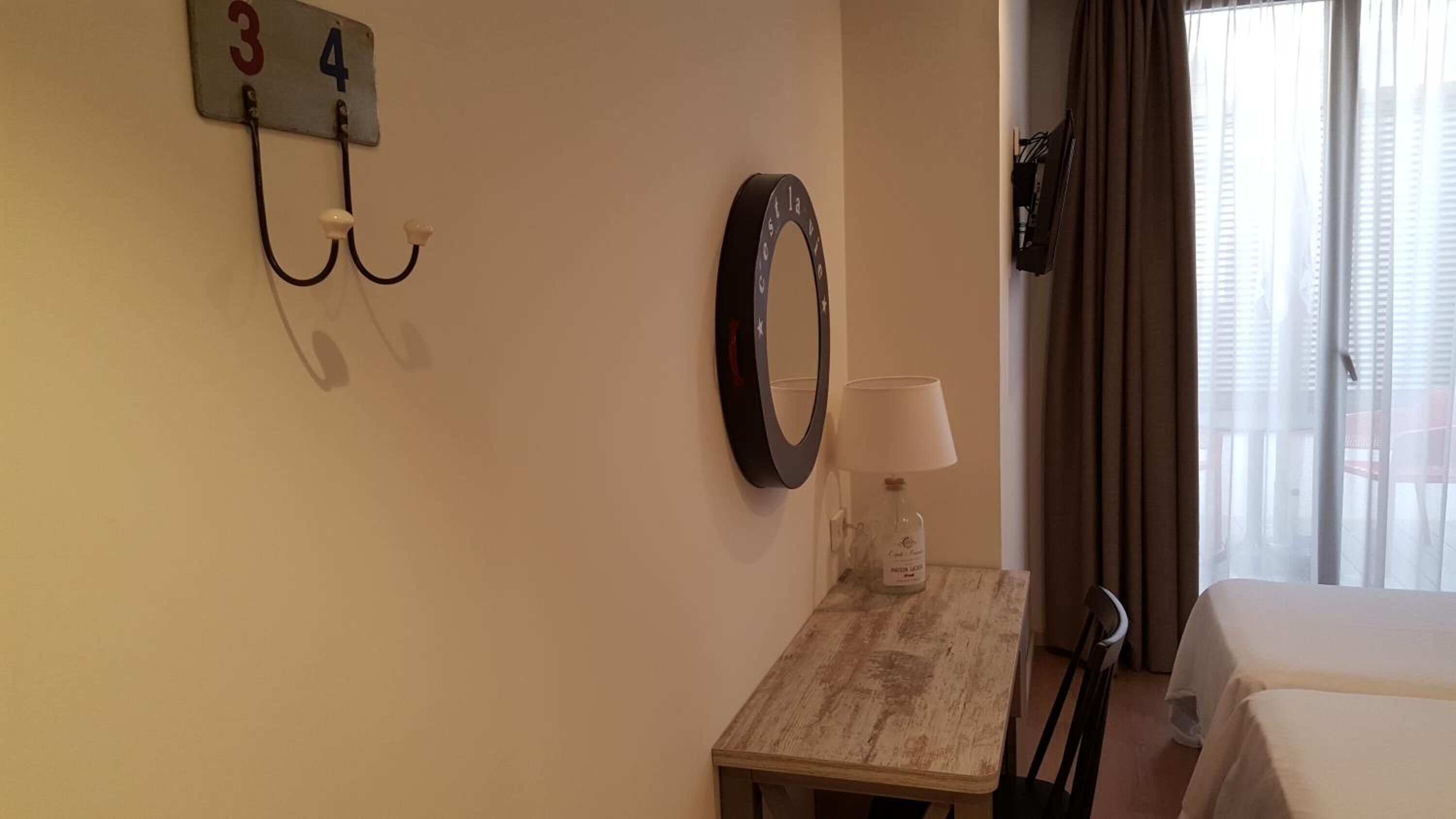 Ett hotellrum med en säng, ett litet bord med en lampa, en spegel och en nummerskylt som är monterad på väggen.