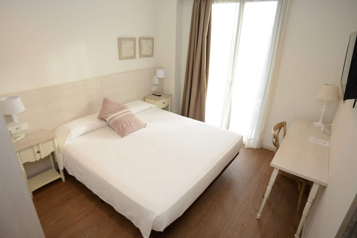 Quarto de hotel com uma cama grande, mesas de cabeceira com luminárias, uma escrivaninha e uma cadeira.