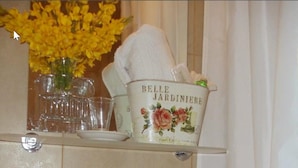 A bathroom with a white sink, two faucets, and a shelf above holding a decorative container and a vase of yellow flowers. - El Molle Hotel Boutique (Sarmiento)
