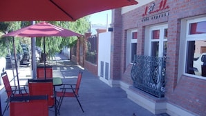 An outdoor cafe area with red chairs and umbrellas, a brick building with a sign reading "Cafe Express," and a metal railing along the building's exterior. - El Molle Hotel Boutique (Sarmiento)