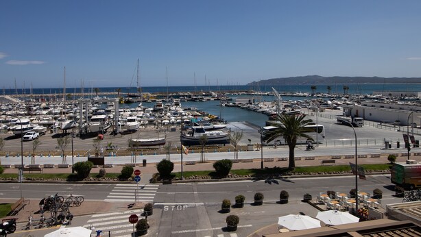 Un port de plaisance où sont amarrés de nombreux bateaux, un passage piéton et une vue dégagée sur la mer.