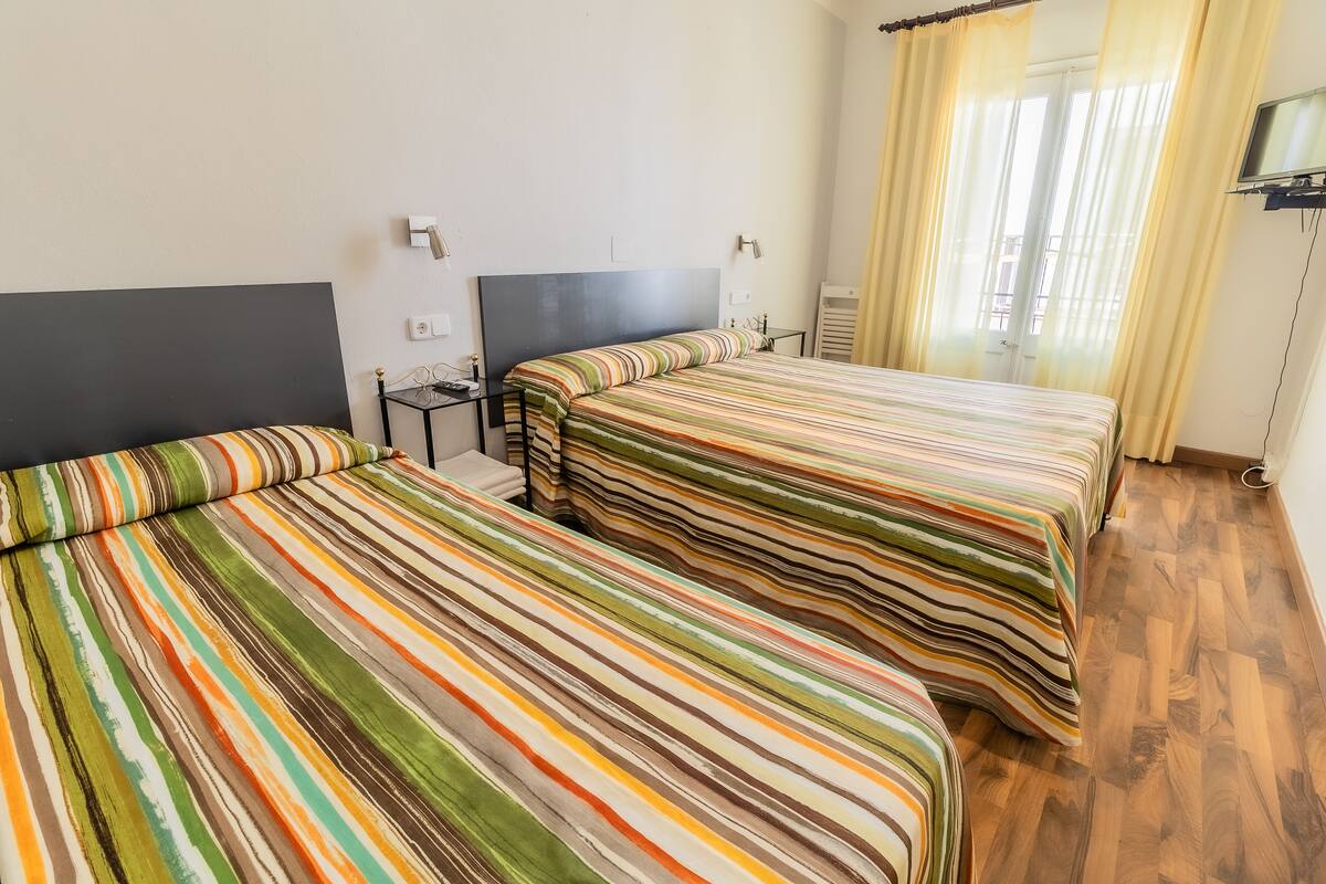 Ein Hotelzimmer mit zwei Betten, einem an der Wand befestigten Flachbildfernseher und einem Fenster mit Vorhängen.