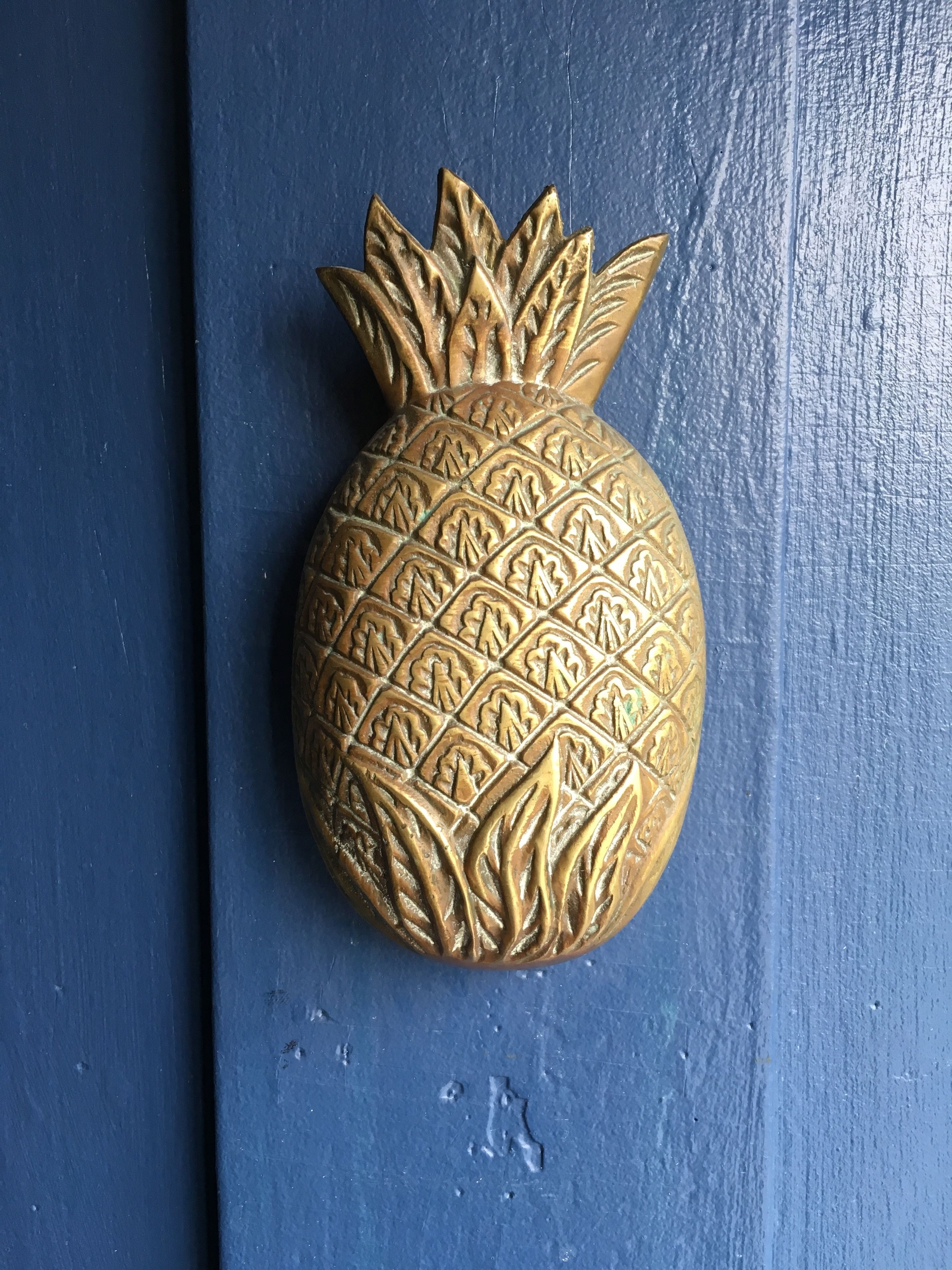 A golden pineapple-shaped door knocker on a blue door.