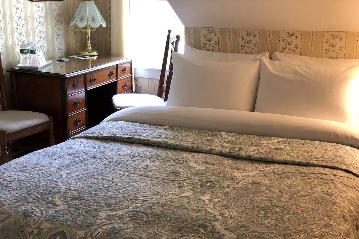 Une chambre à coucher avec un lit, une table de chevet en bois, une lampe et une chaise.