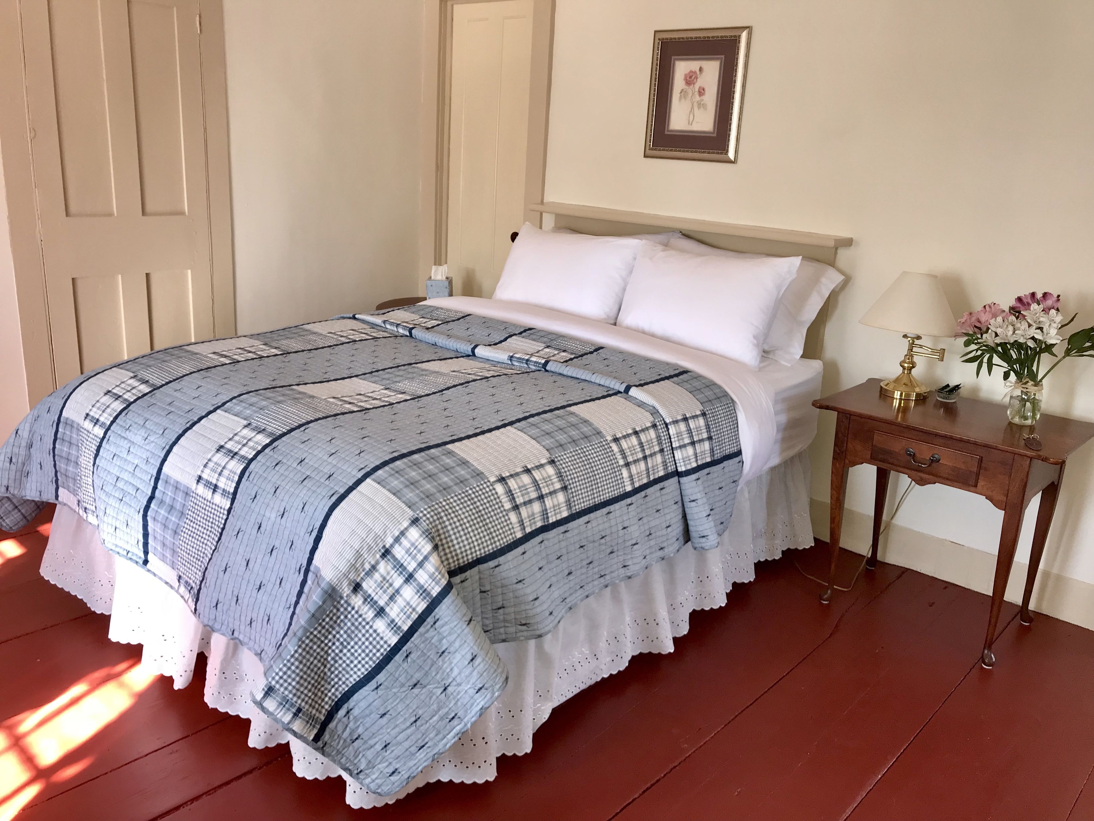 A bedroom with a bed, a nightstand, a lamp, and a vase with flowers.