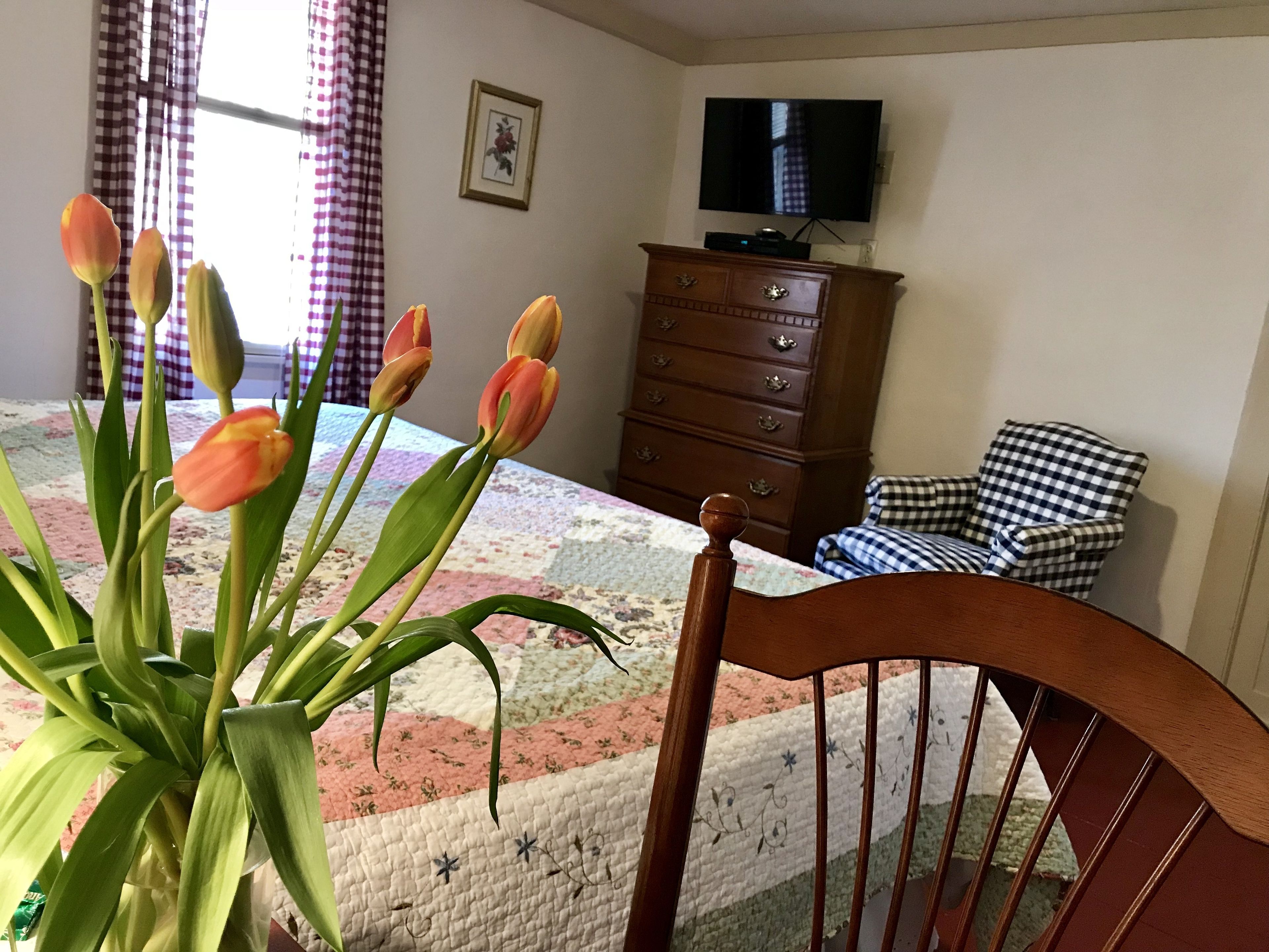 A bedroom with a bed, a wooden dresser, a television, and a chair.