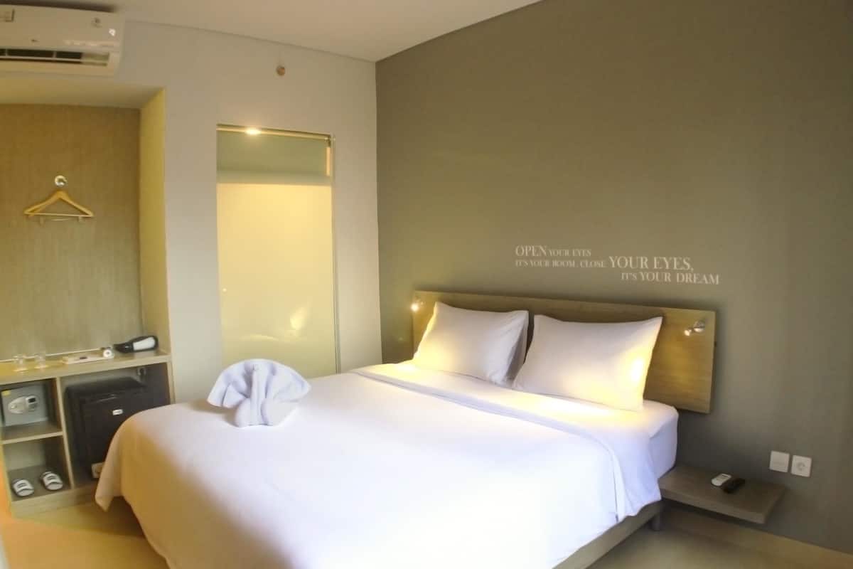 A hotel room with a large bed, a bedside table, a mirror, and a wall with motivational text.