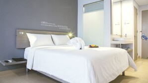 A modern hotel room with a neatly made bed, a bedside table with a remote control, and a wall-mounted mirror. - Kyriad Hotel Fatmawati - Jakarta (Jakarta)
