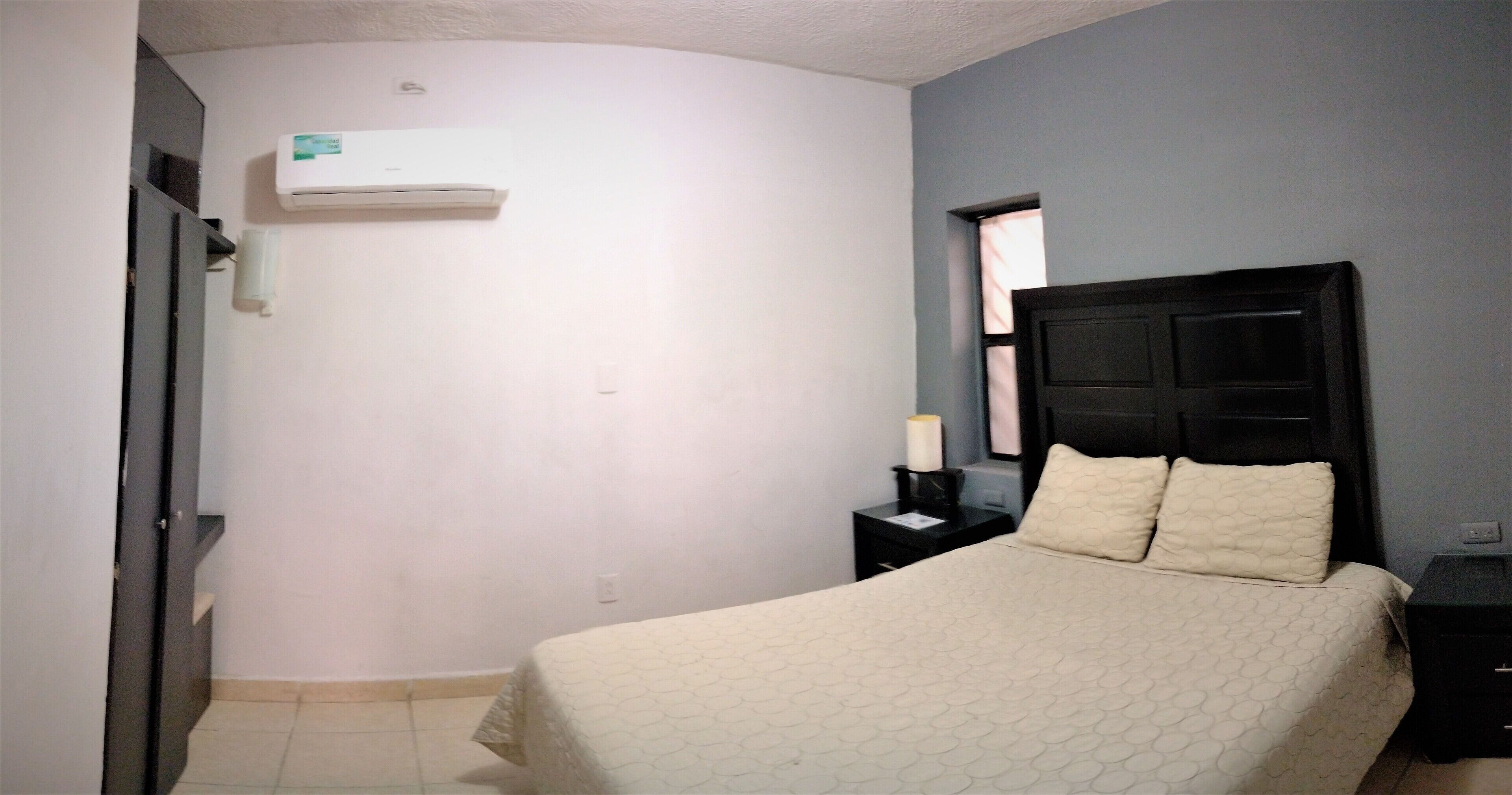 Un dormitorio con cama, mesita de noche, ventana y aire acondicionado.