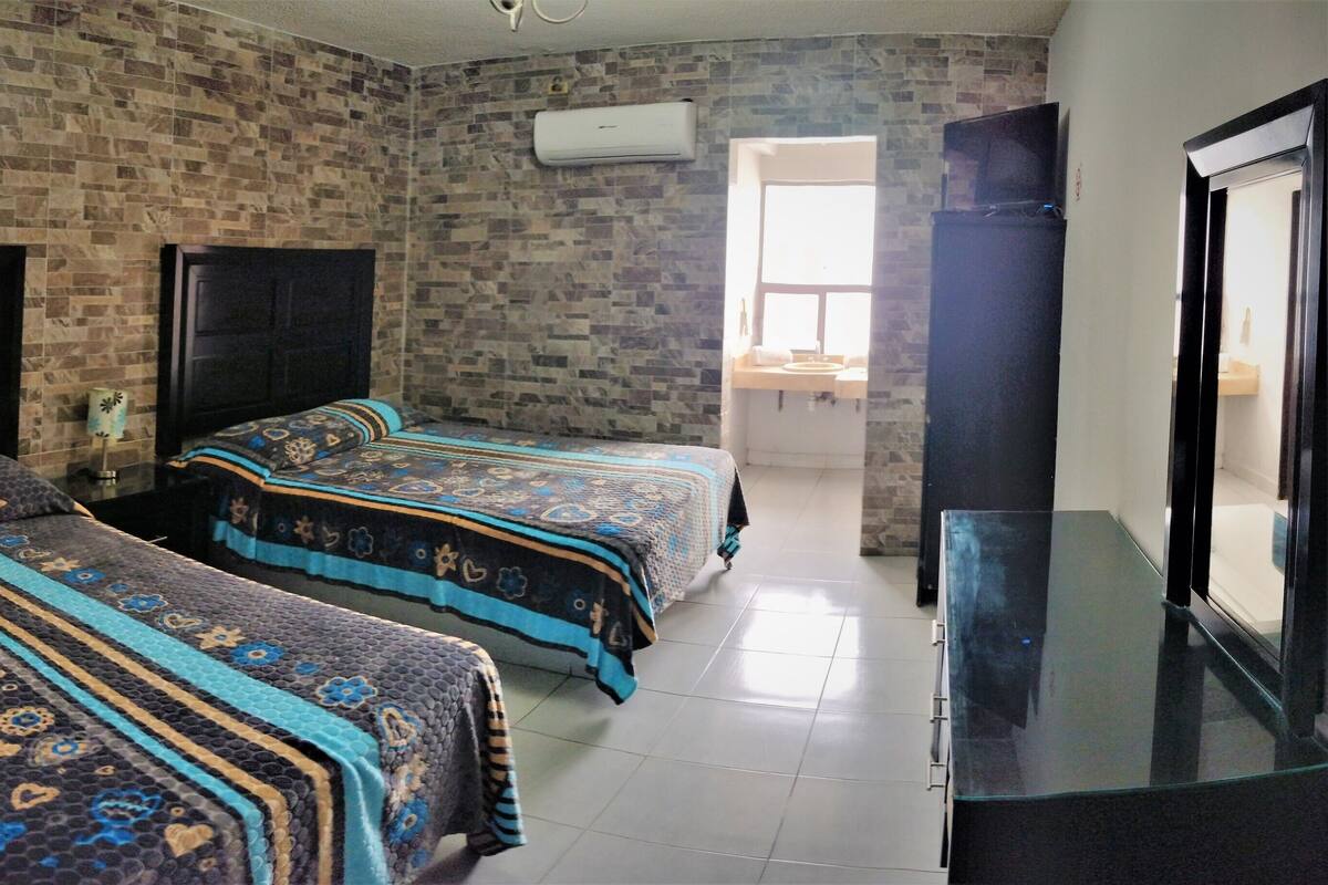 A room with two beds, a TV, and a brick wall.