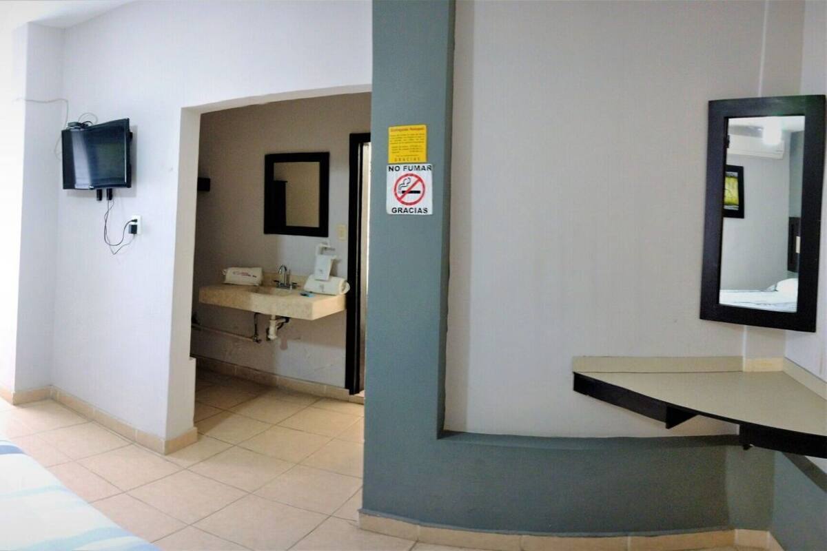 A hotel room with two beds, a TV, a bathroom with a sink, and a mirror.