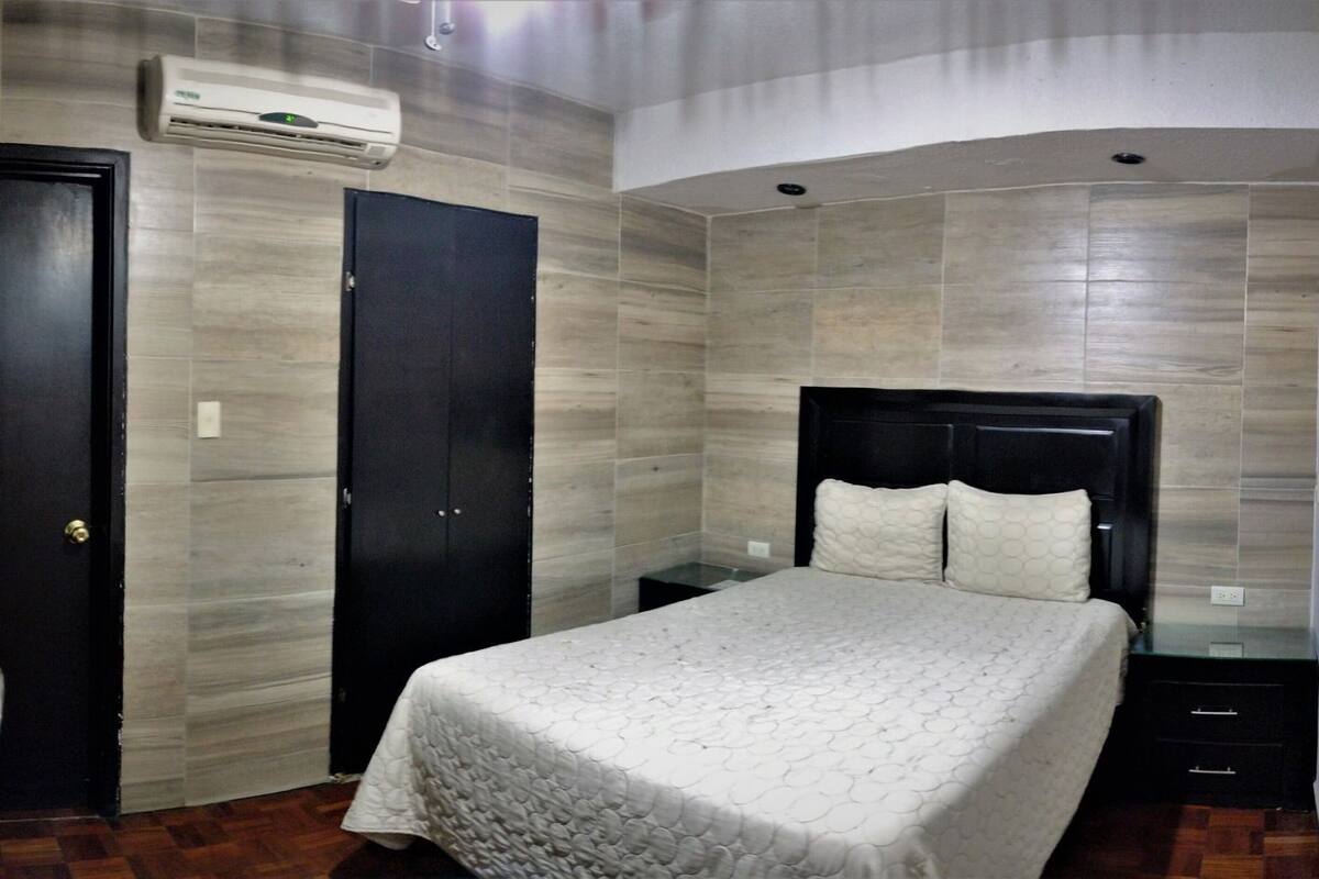 A bedroom with a bed, a wardrobe, a nightstand, and an air conditioning unit.
