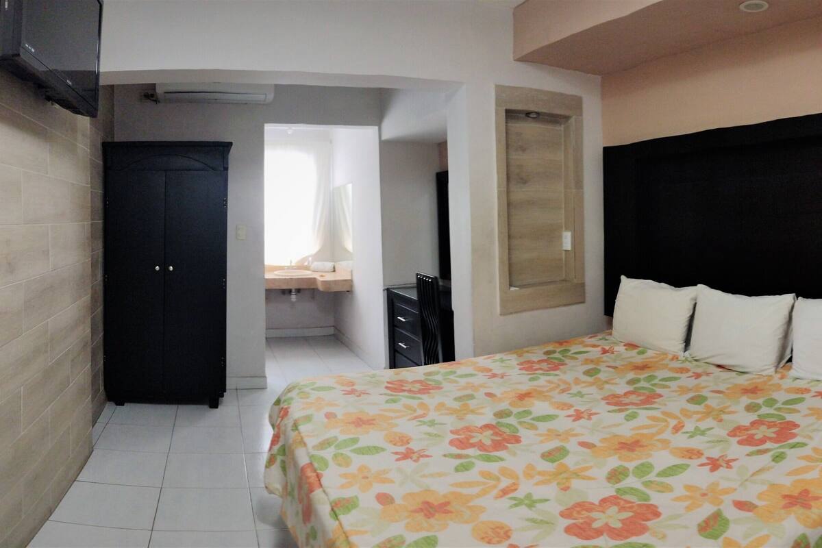 A bedroom with a bed, a nightstand, a desk, and a wardrobe.