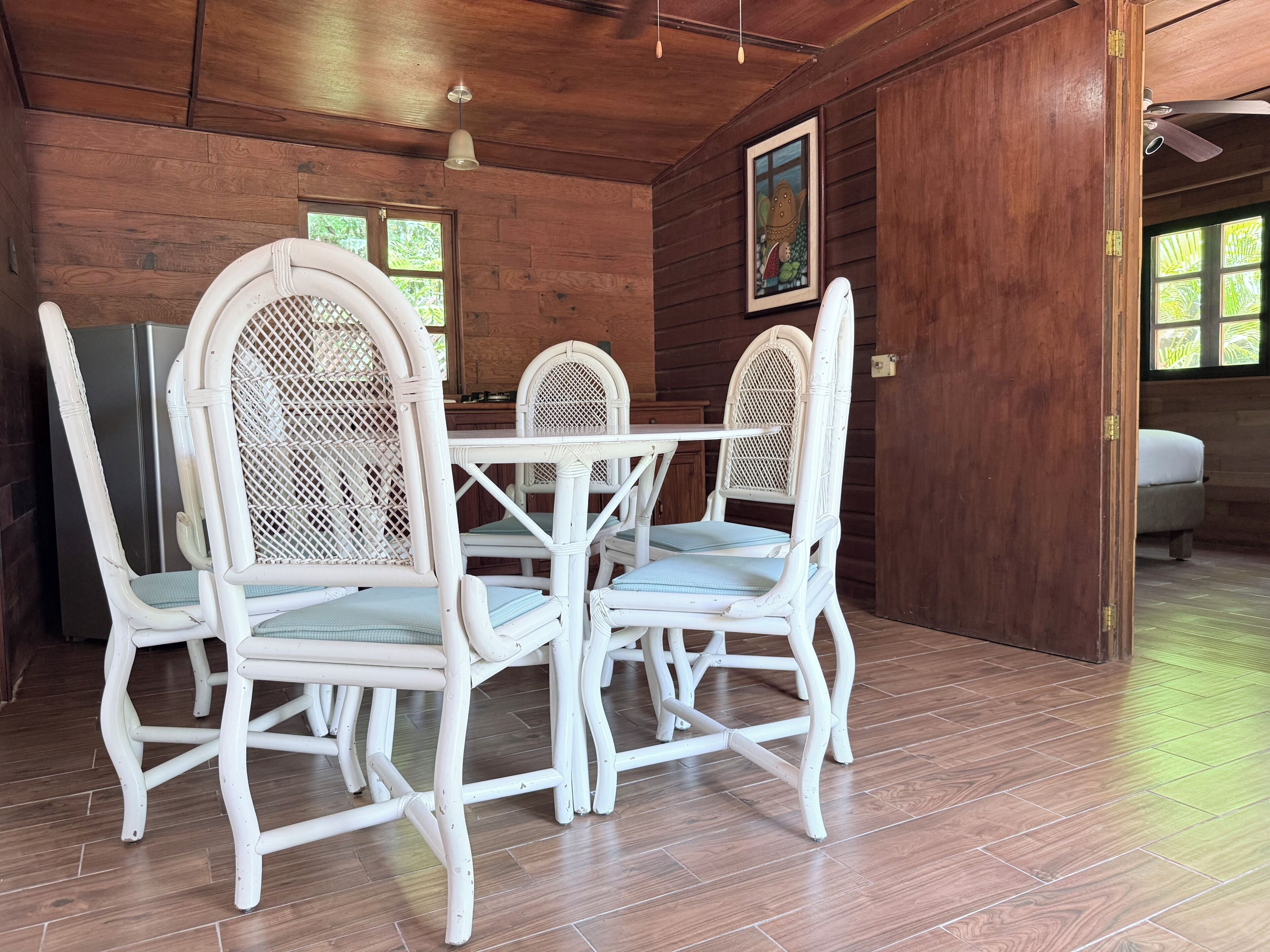 A dining area with white wicker chairs and a table, wooden walls, and a ceiling fan.