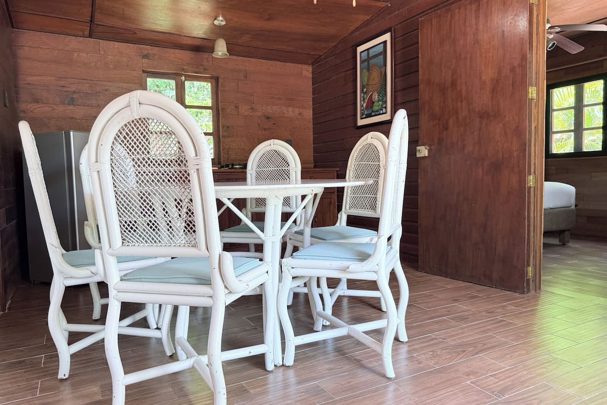 A dining area with white wicker chairs and a table, wooden walls, and a ceiling fan.