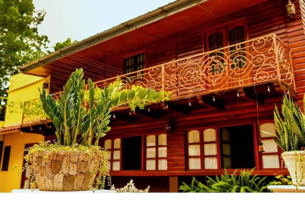 A wooden house with a balcony, potted plants, and a stone wall.