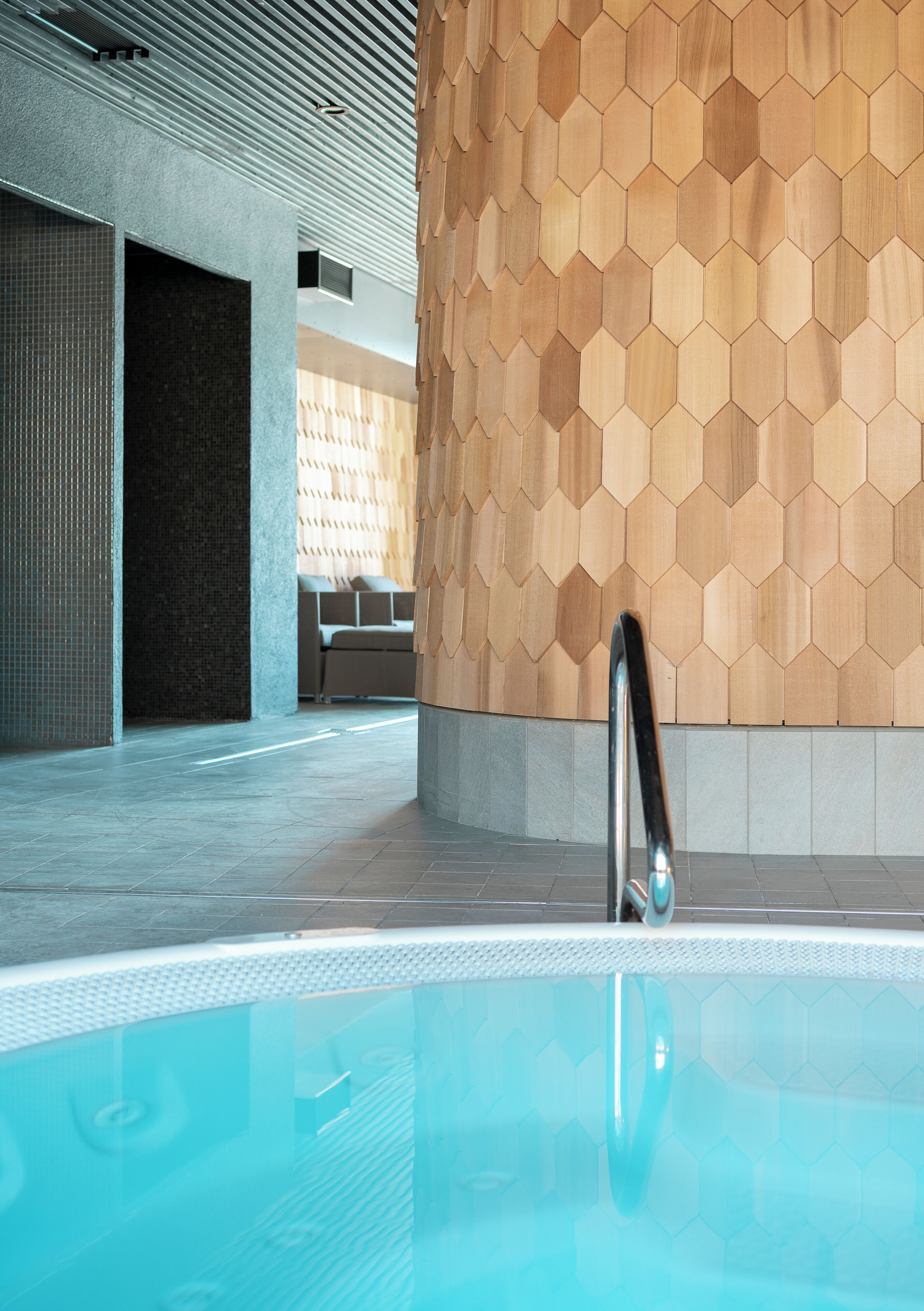 Un área de piscina interior moderna con un muro hexagonal de madera y una piscina transparente.