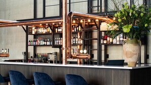 A bar area with copper pipes, bar stools, and shelves of bottles.