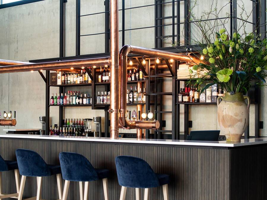 A bar area with copper pipes, bar stools, and shelves of bottles.