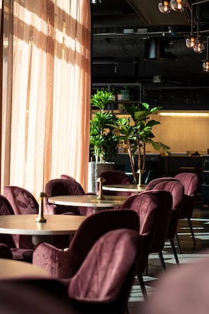 A restaurant with round tables and purple chairs, a potted plant, and a wooden column.