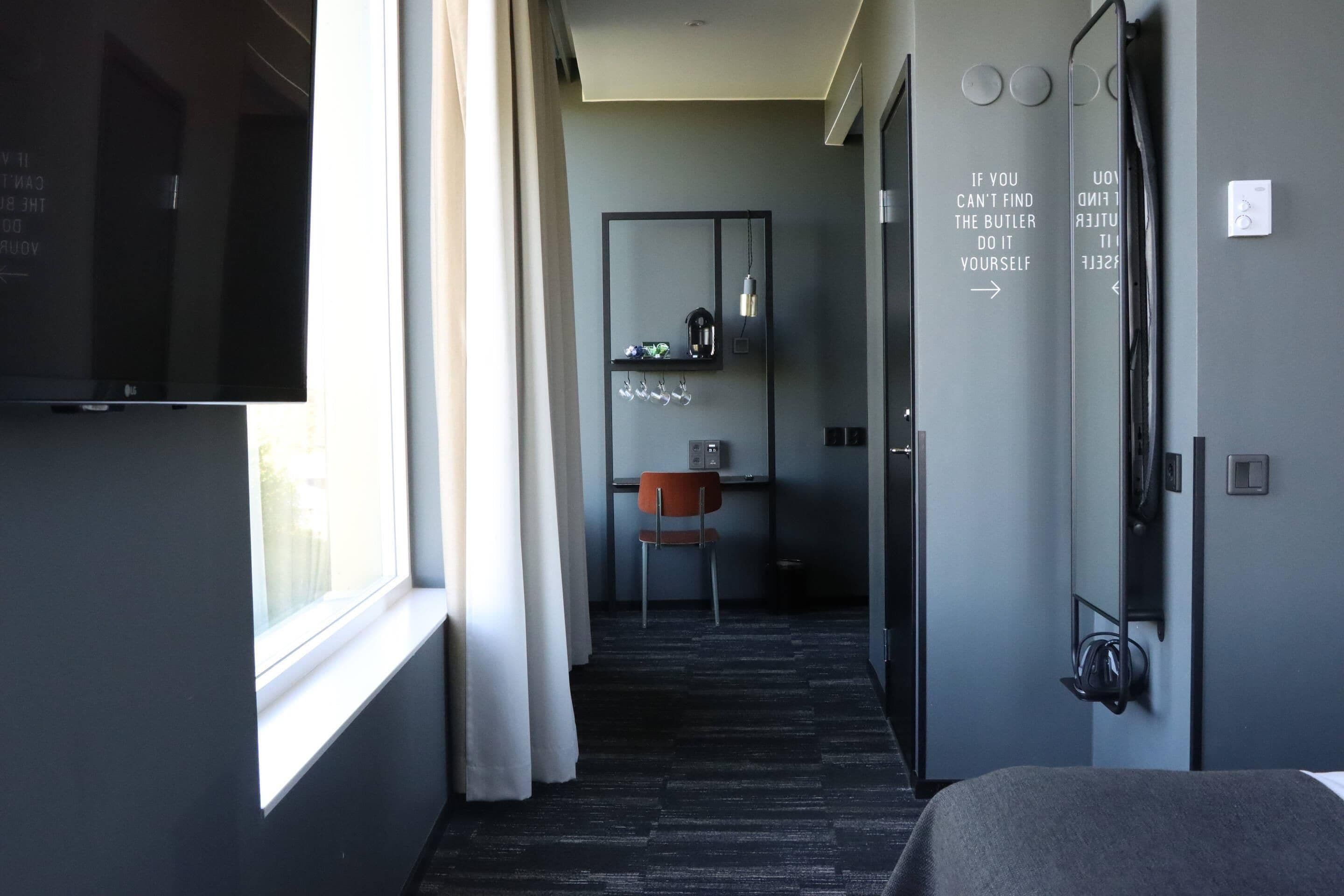 A modern hotel room with a bed, a TV, a chair, and a desk with a mirror.