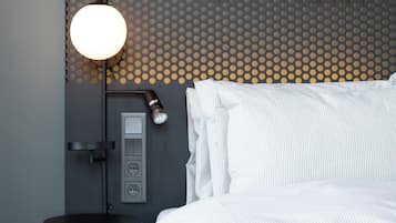 Habitación de hotel moderna con cama, escritorio y lámpara de pared. Un cartel indica que el gimnasio y la recepción están abiertos las 24 horas, todos los días.
