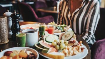 Una mesa de comedor con alimentos para el desayuno, incluyendo frutas, queso y bebidas.