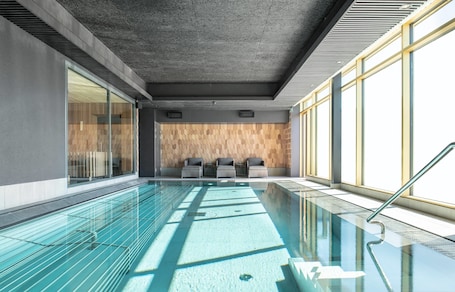 A modern indoor swimming pool with clear glass walls, a wooden wall with geometric patterns, and a seating area with chairs.. Quality Hotel The Box