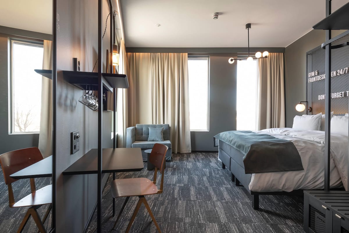 Una habitación de hotel con cama, escritorio, silla, sofá y un gran ventanal.