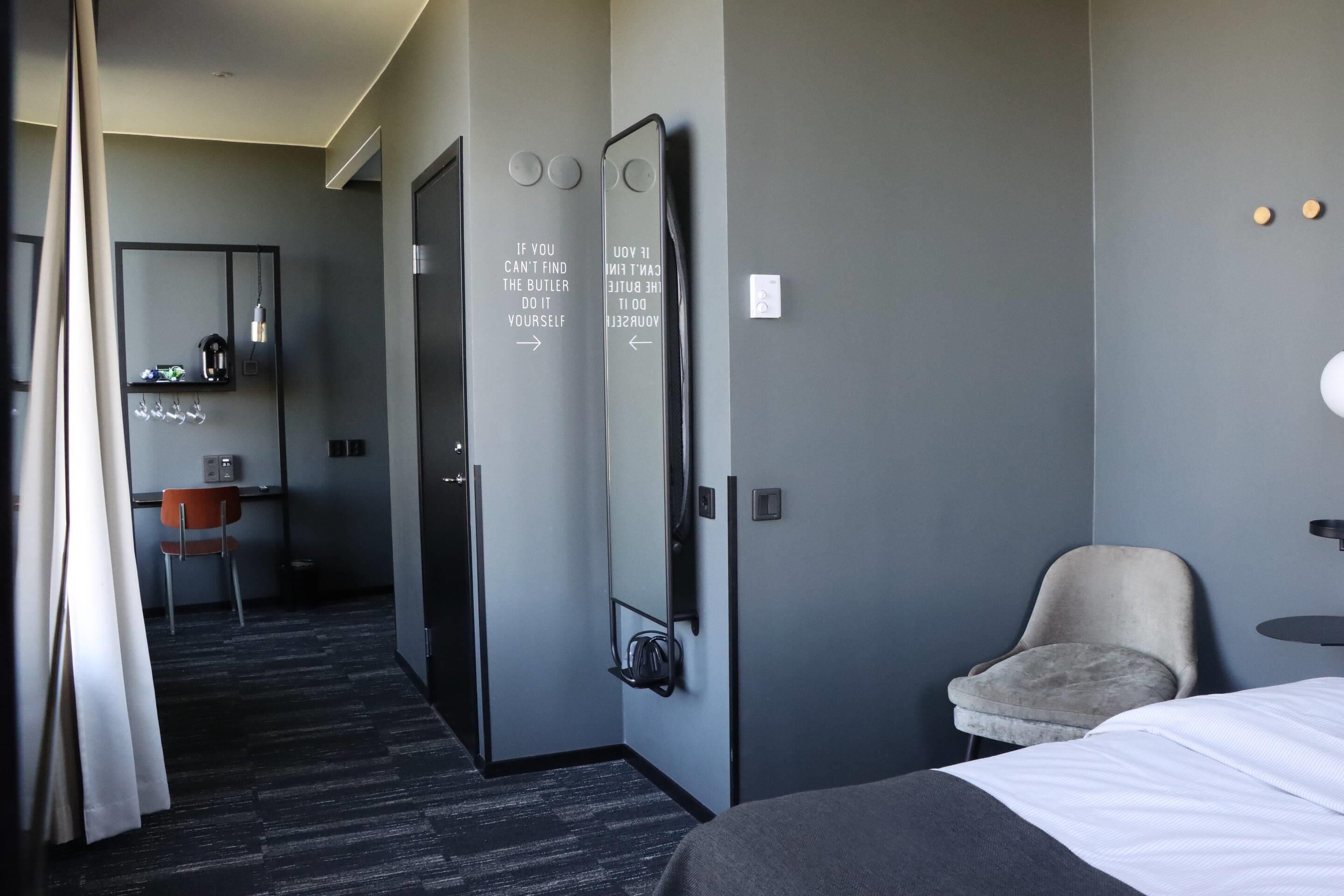 A hotel room with a bed, a chair, a desk, and a mirror with motivational text.