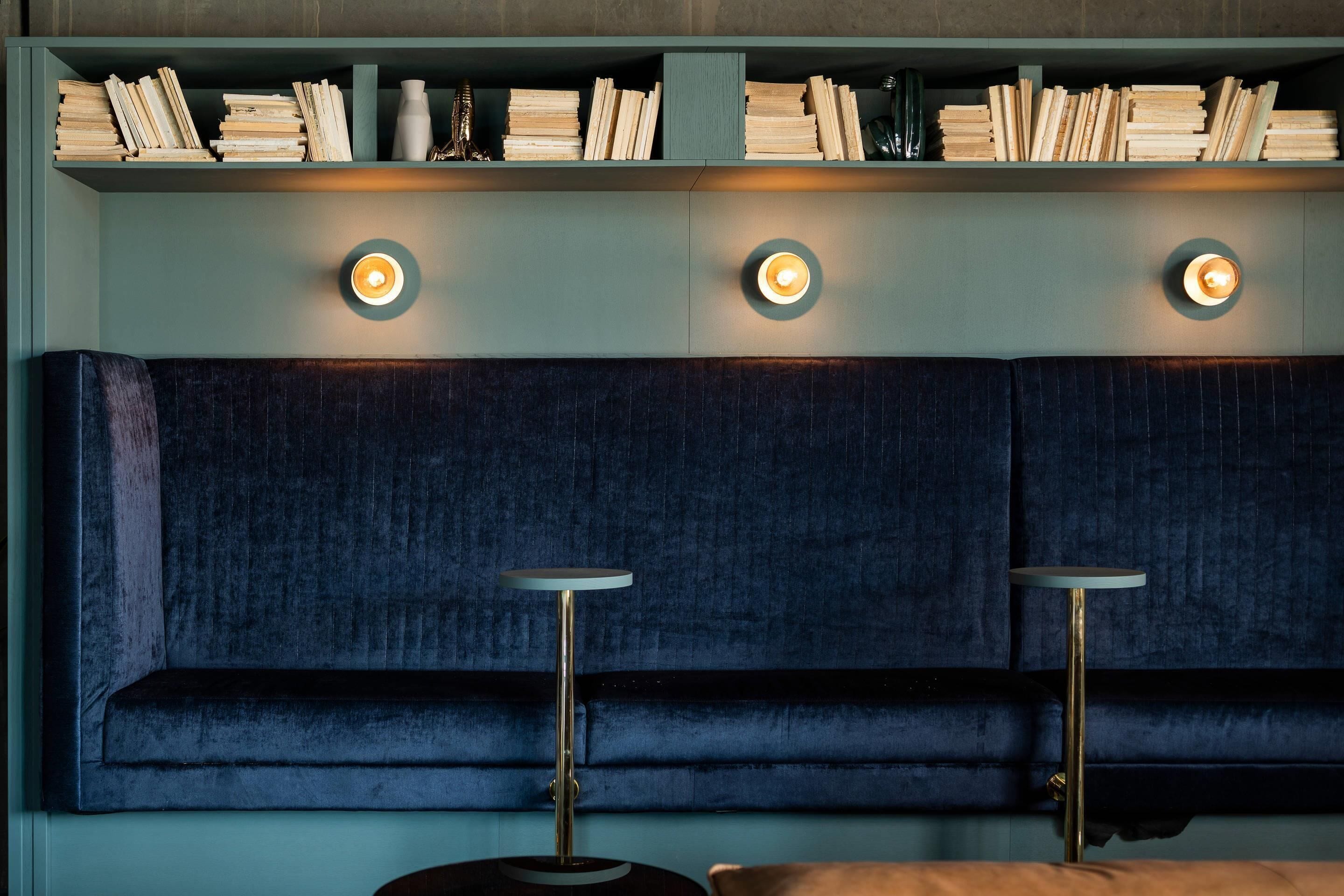 A room with a dark blue upholstered headboard, a bookshelf with books, and two floor lamps.
