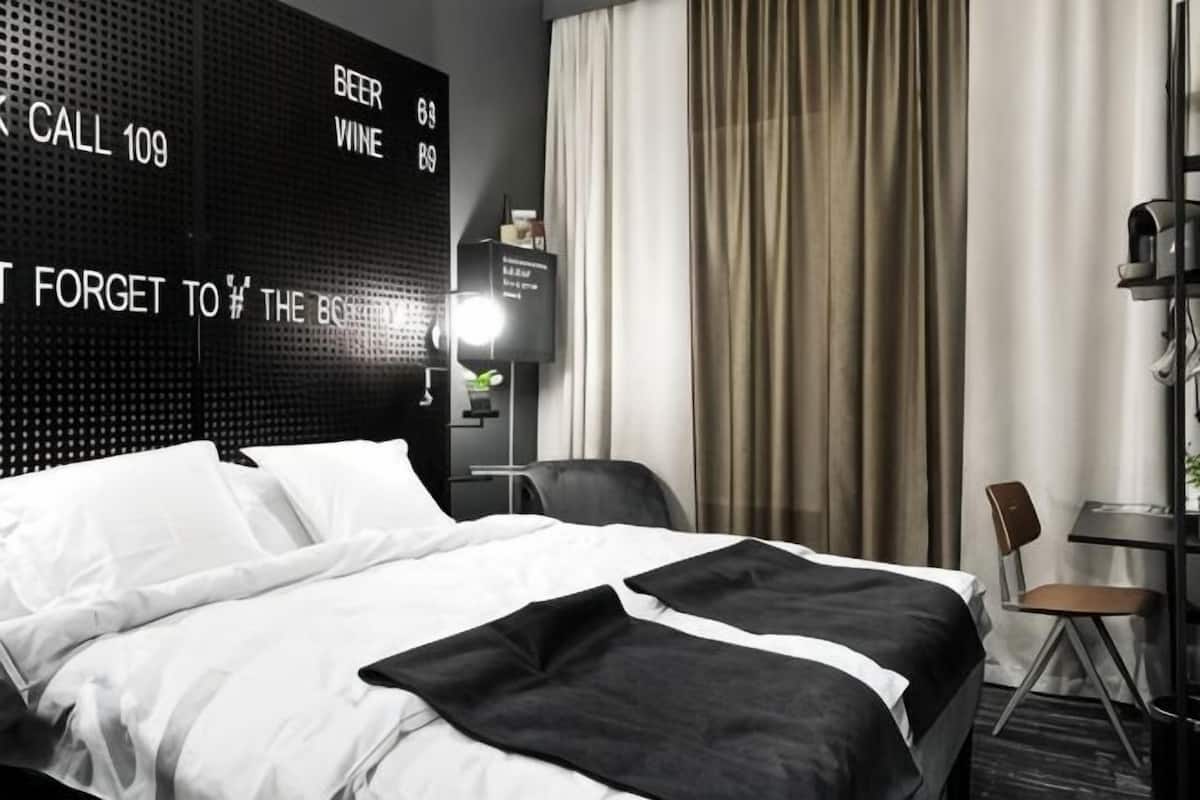 Habitación de hotel con cama, escritorio, silla, televisor y una pared con pantalla digital.