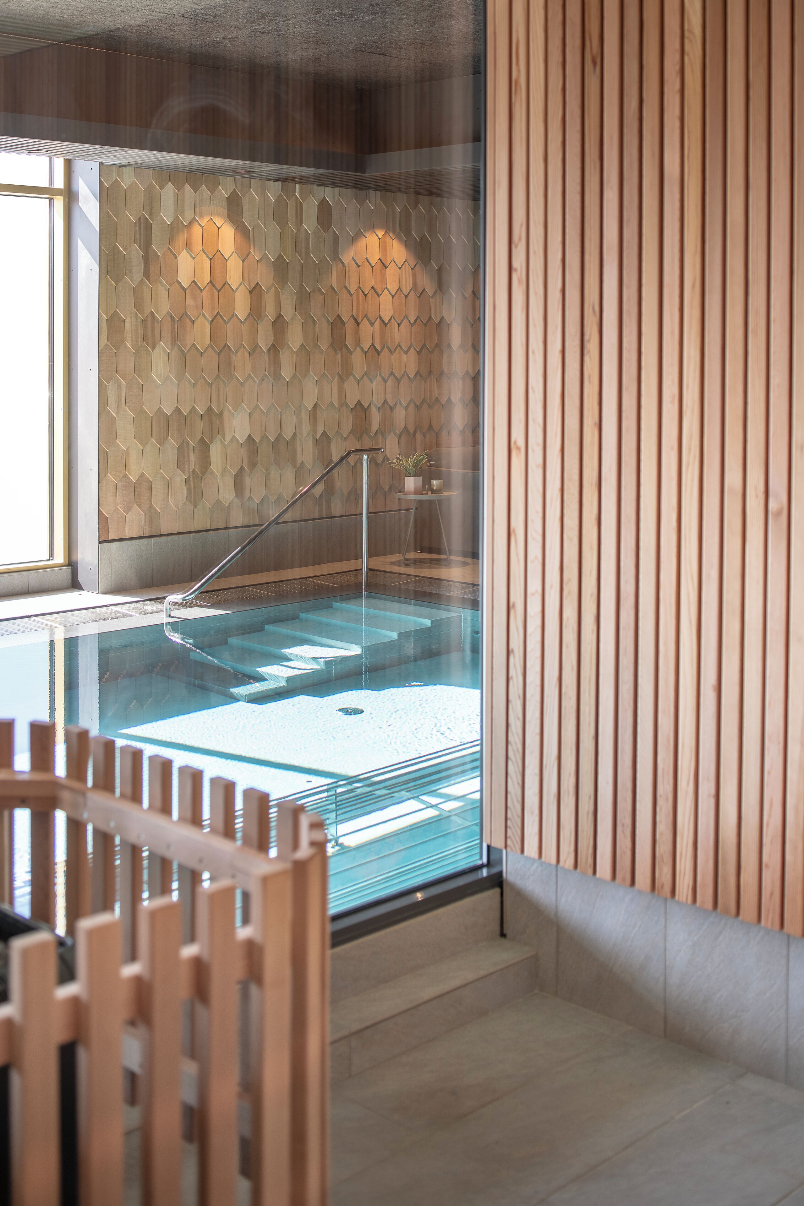 A modern spa area with a glass-enclosed hot tub, wooden panel walls, and a clear view of the outside.