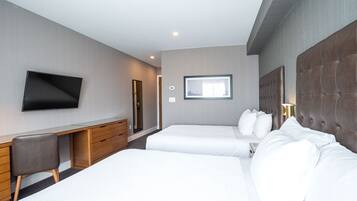 A hotel room with two beds, a desk, a flat-screen TV, and a window.