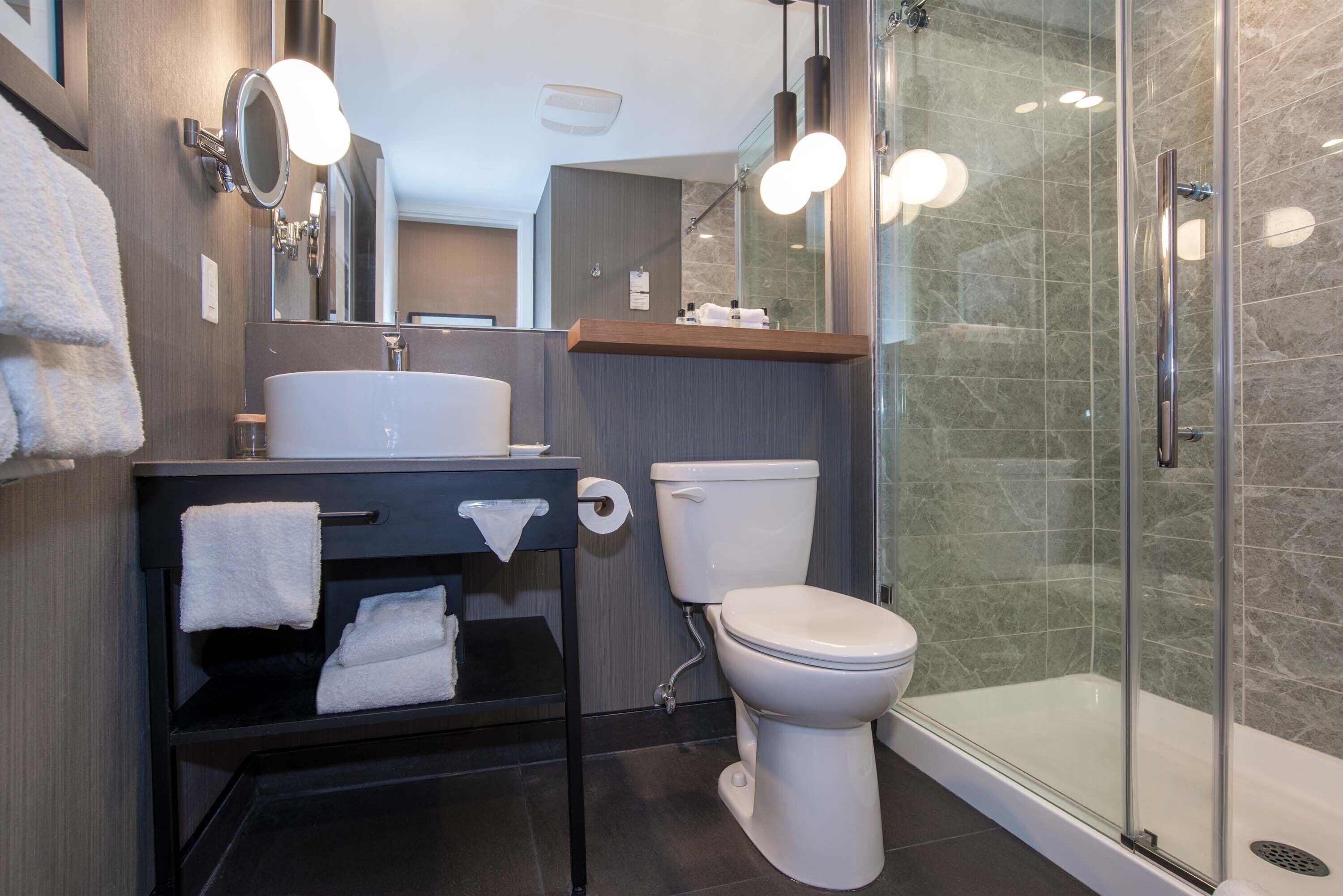 Une salle de bain moderne avec une douche à parois de verre, des toilettes blanches et un meuble-lavabo noir doté d’un miroir et d’un porte-serviettes.
