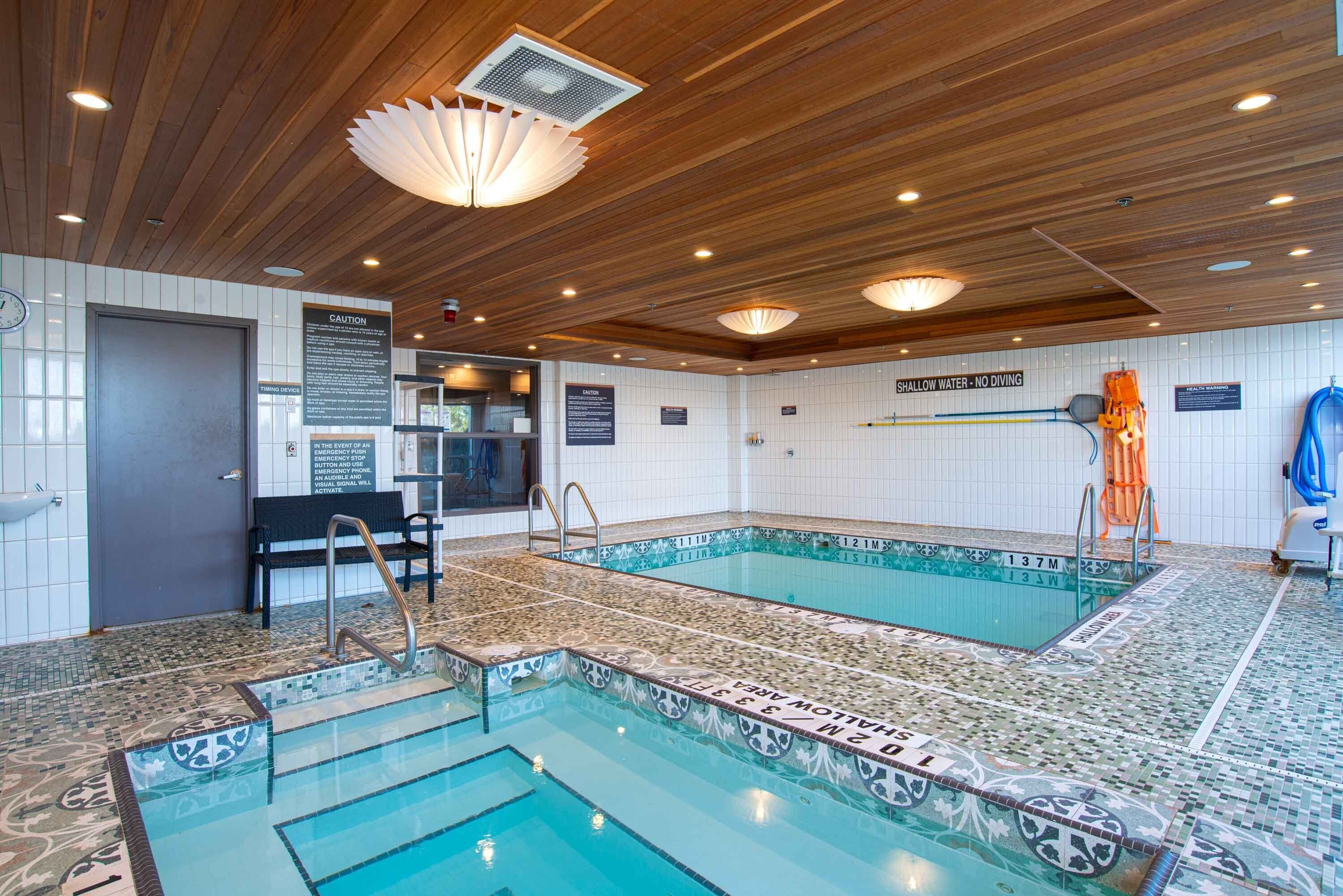 Une piscine intérieure avec des murs carrelés et un plafond en bois, équipée d’un banc et de panneaux de signalisation de sécurité.