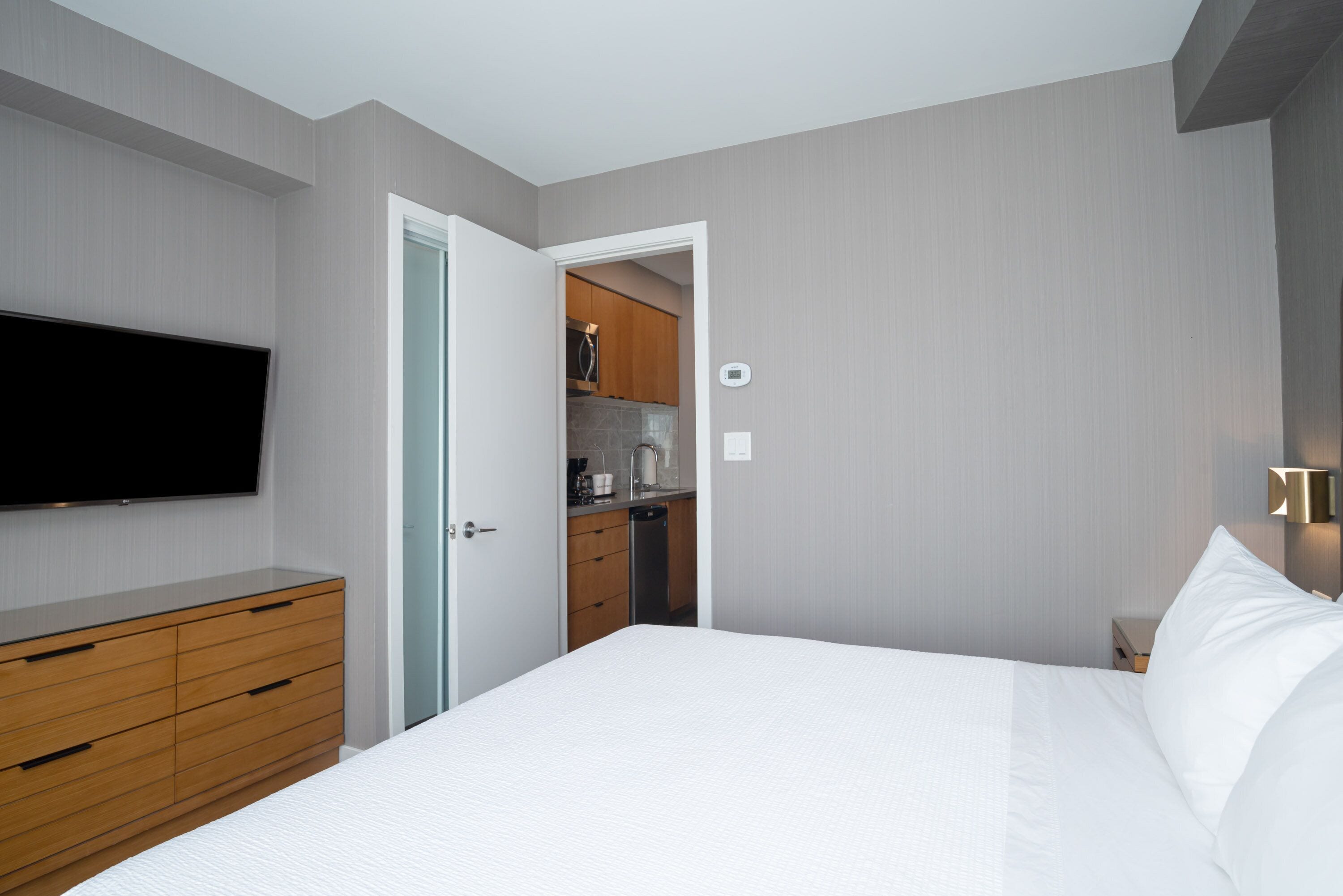 Una habitación de hotel moderna con una cama grande, cómoda de madera y un televisor de pantalla plana en la pared.